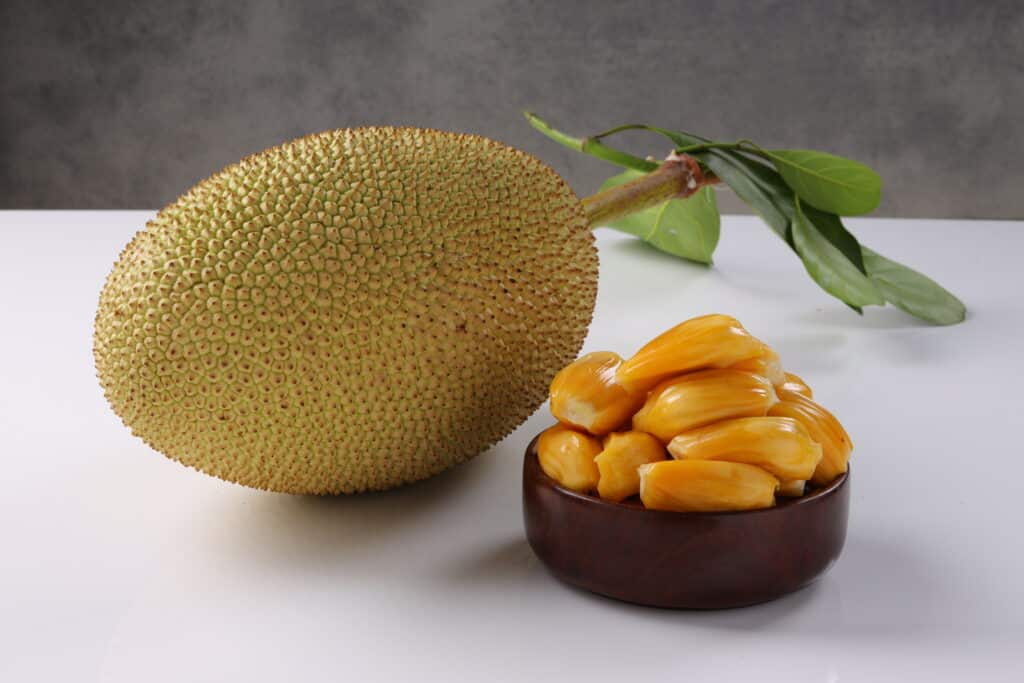 Tout ce que vous devez savoir sur le jacquier : préparation, recettes et bienfaits 3 Fruit du jacquier mûr joliment disposé dans un bol en bois sur fond blanc texturé.